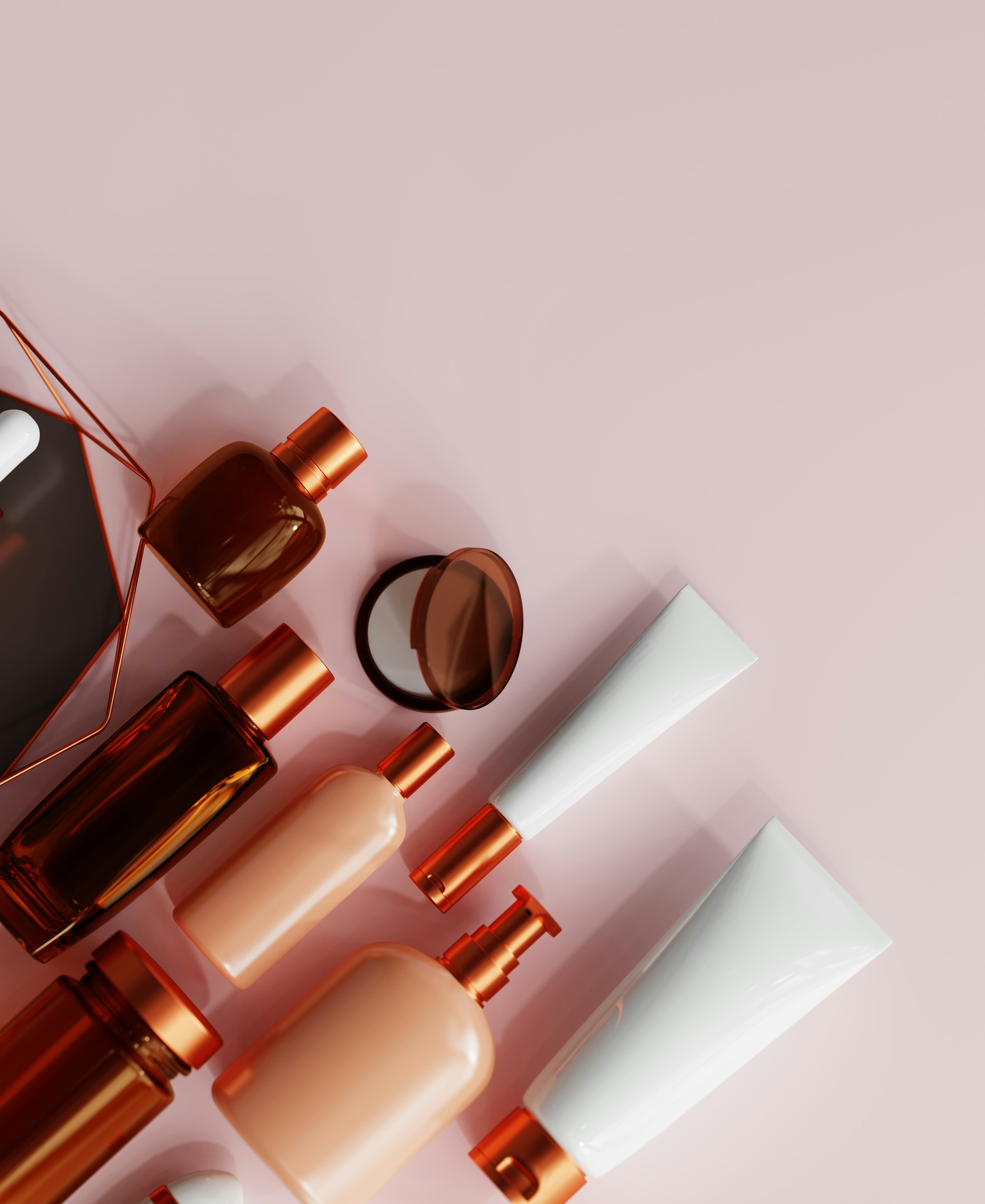 Flat lay of amber and blush glass bottles with copper caps, a compact and white tubes on a pale pink background.