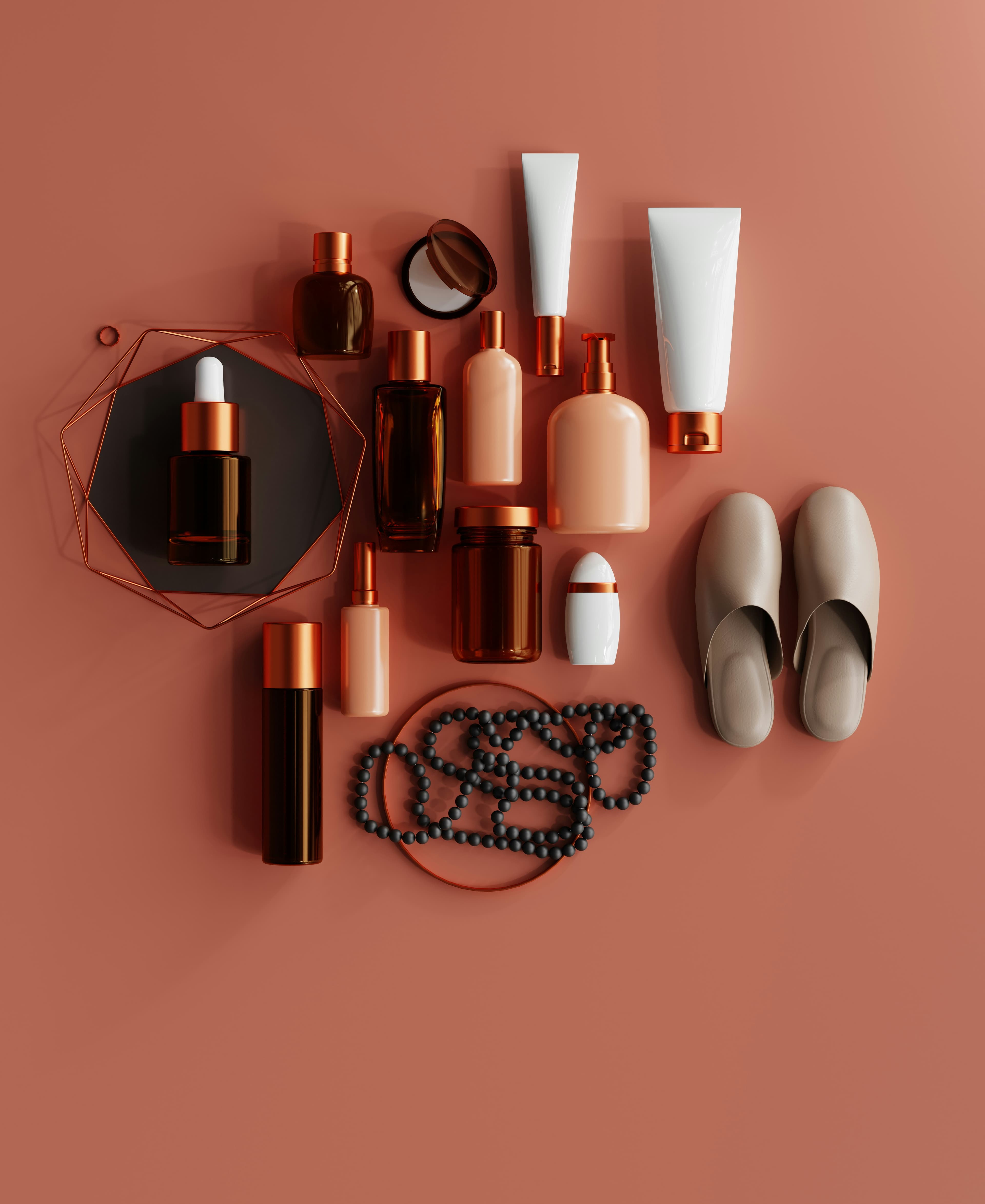Flat lay of amber bottles, blush pump bottles, white tubes, beads and slippers on a terracotta surface.