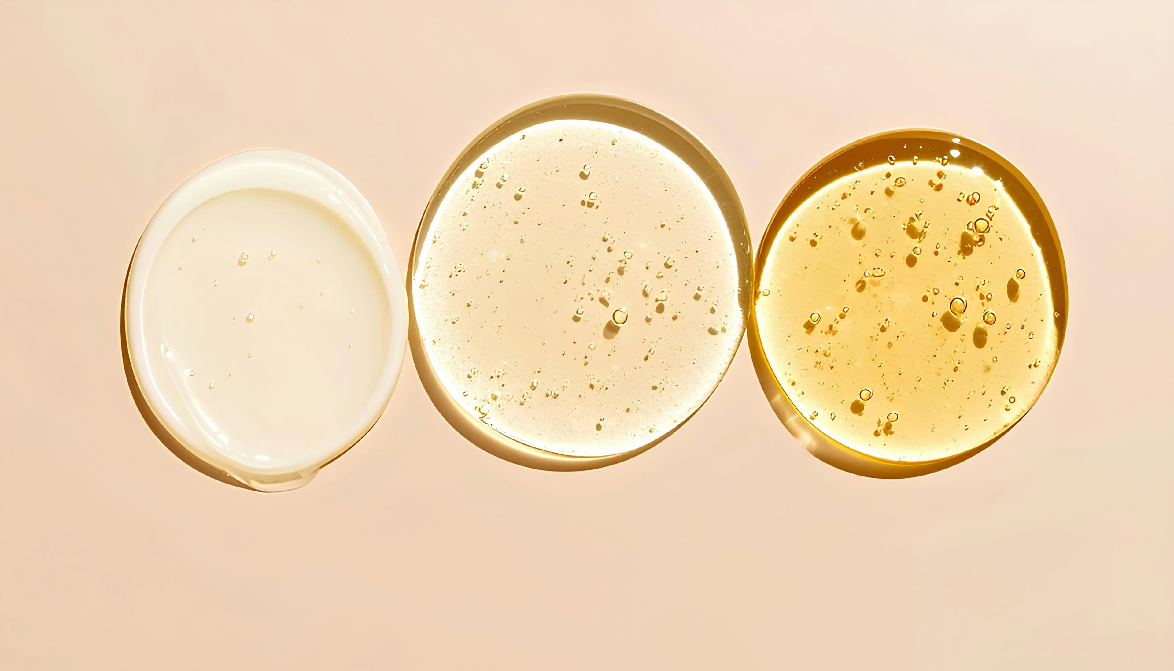 Three round swatches of cream, gel and golden oil in a row on a peach background.